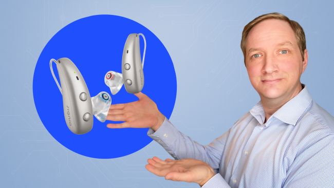 Maximilian Bauer zeigt zwei Signia Pure Charge&Go MaX Hörgeräte mit individuell gefertigten Otoplastiken